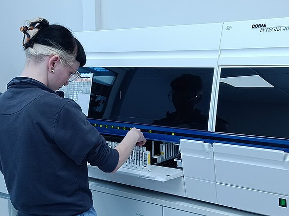 Eine TFA bestückt ein Laborgerät mit Blutproben, die untersucht werden sollen. 