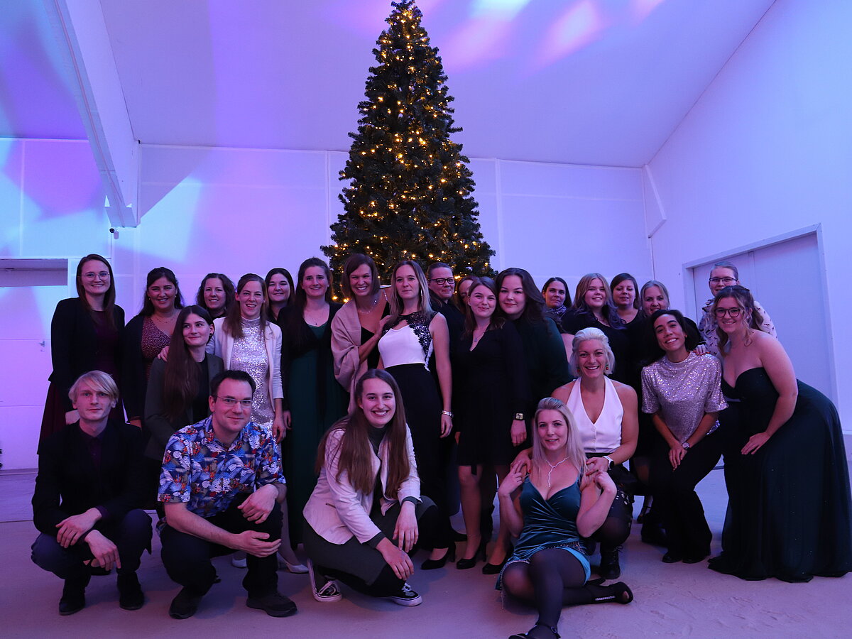 Hier sieht man das Ambulanzteam der Tiermediznischen Fachangestellten während unserer Weihnachtsfeier. Alle tragen festliche Kleidung und sitzen vor einem Weihnachtsbaum. 