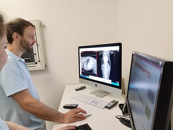 Hier sieht man Dr. Jan Wennemuth, der vor zwei Bildschirmen steht, und CT-Bilder befundet.