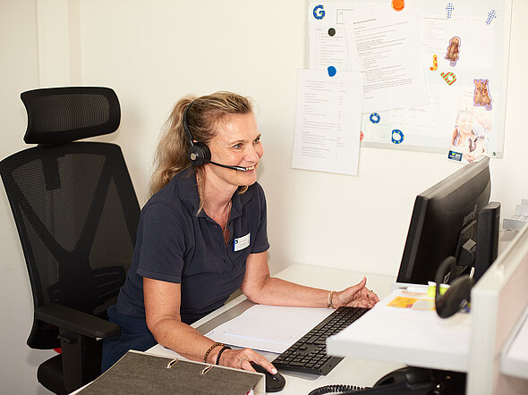 Dieses Bild zeigt eine Mitarbeiterin unserer Telefonzentrale, die mit Headset telefoniert. Dabei tippt sie die erforderlichen Daten in einen Computer ein.